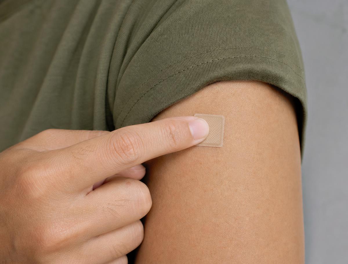 Microneedle vaccine patch applied to the arm of a person in an army-green t-shirt