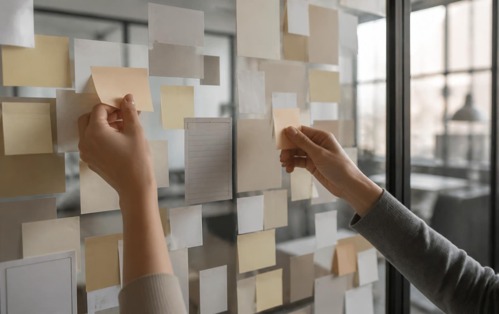 Two people clustering research notes into affinity groups on a glass wall
