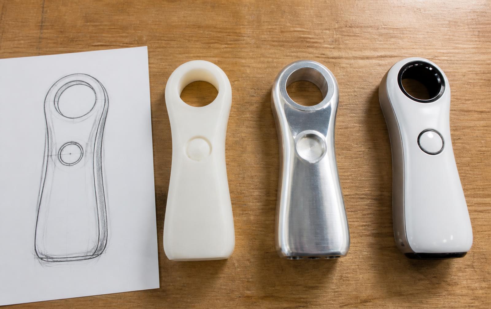Bench showing a sketch, a 3D printed housing, a machined prototype and a finished device side by side