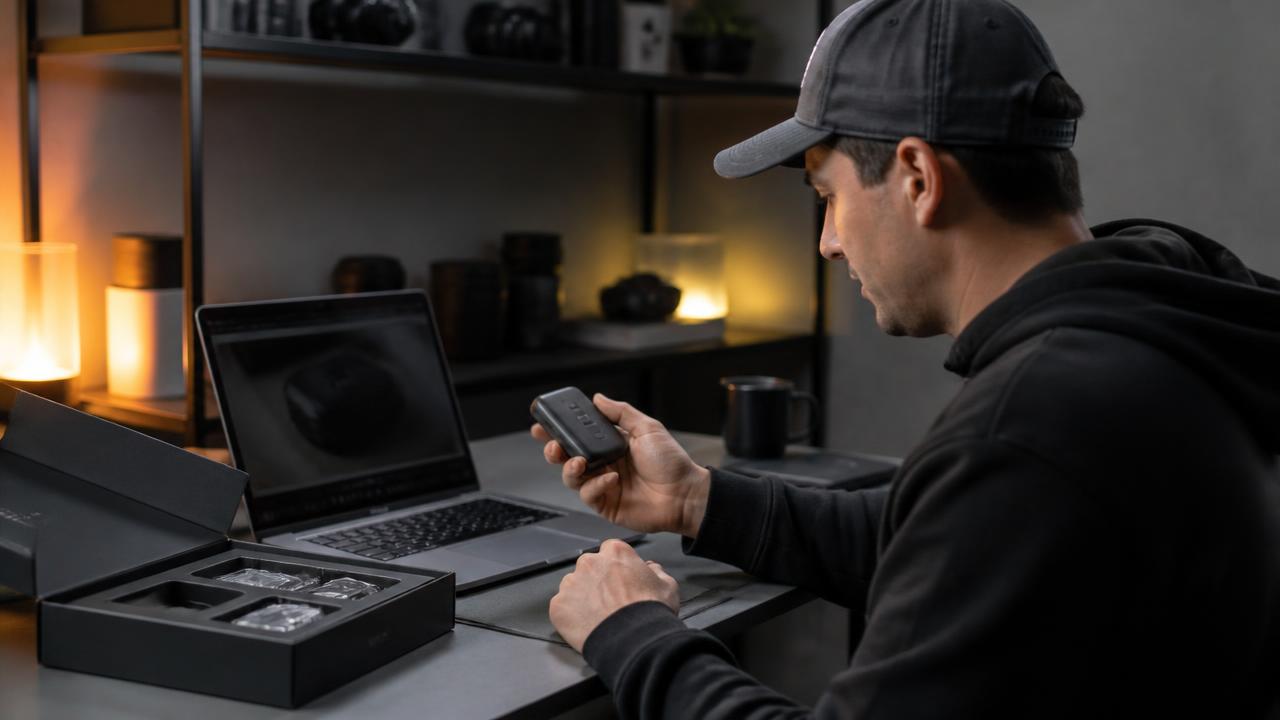 Person unboxing a new hardware device at a desk while writing an online review on a laptop