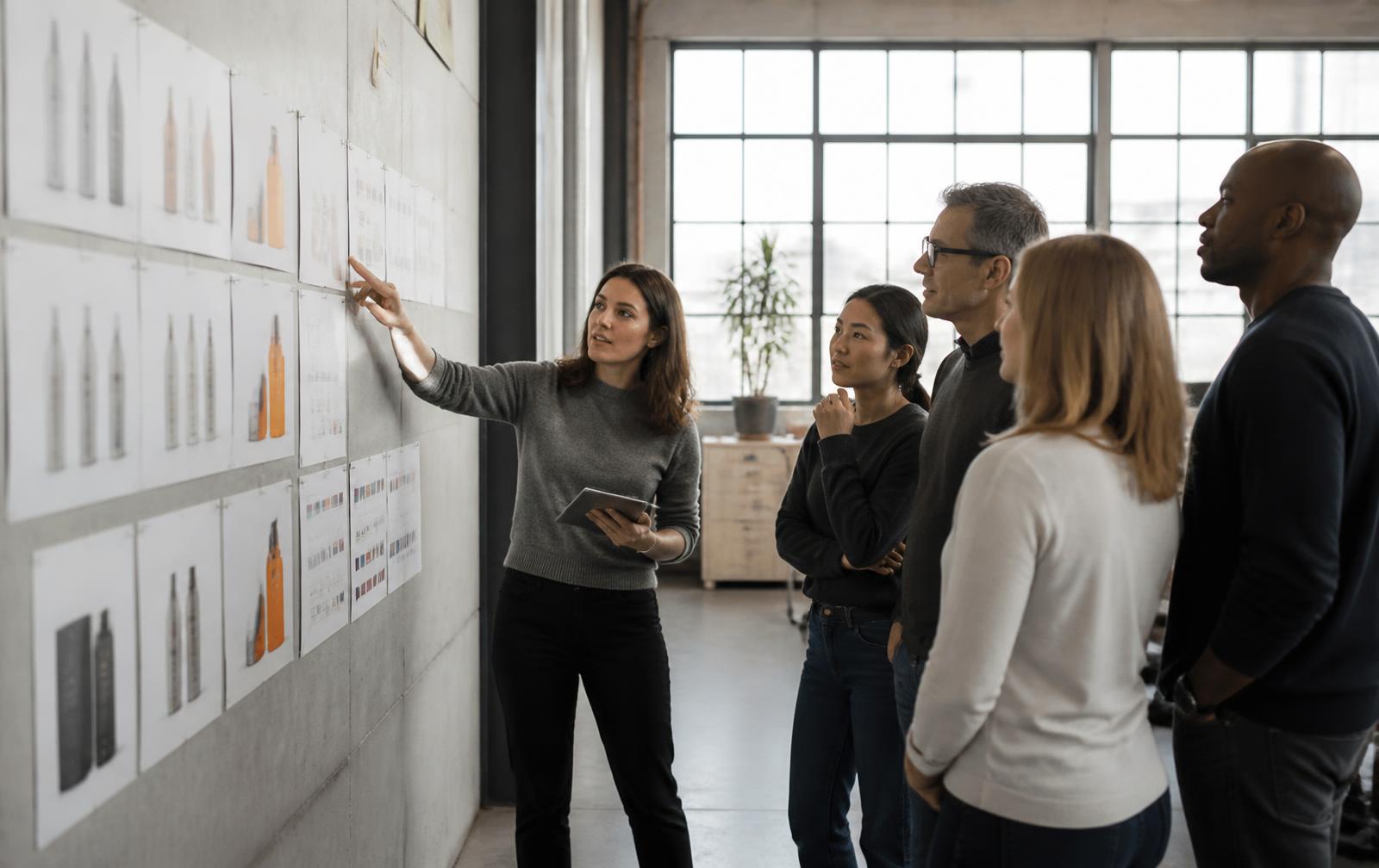 Product marketing team reviewing packaging mockups and a launch timeline pinned to a studio wall
