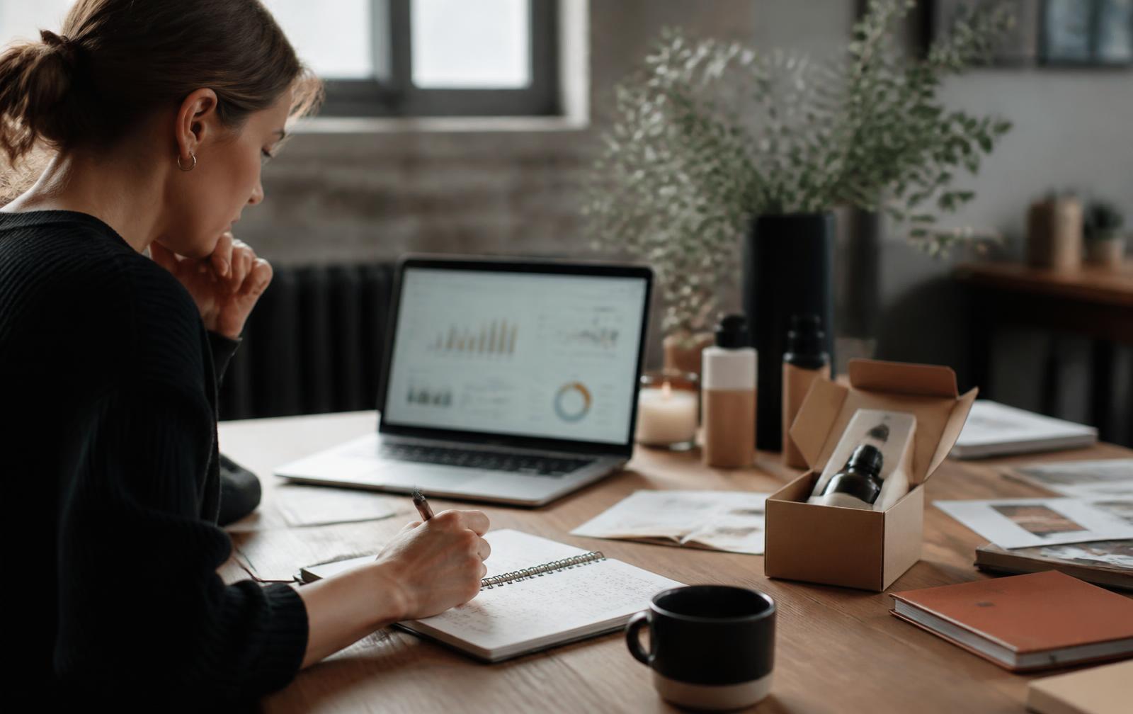 Marketer planning an invention launch with analytics on a laptop and a packaged product sample on the desk