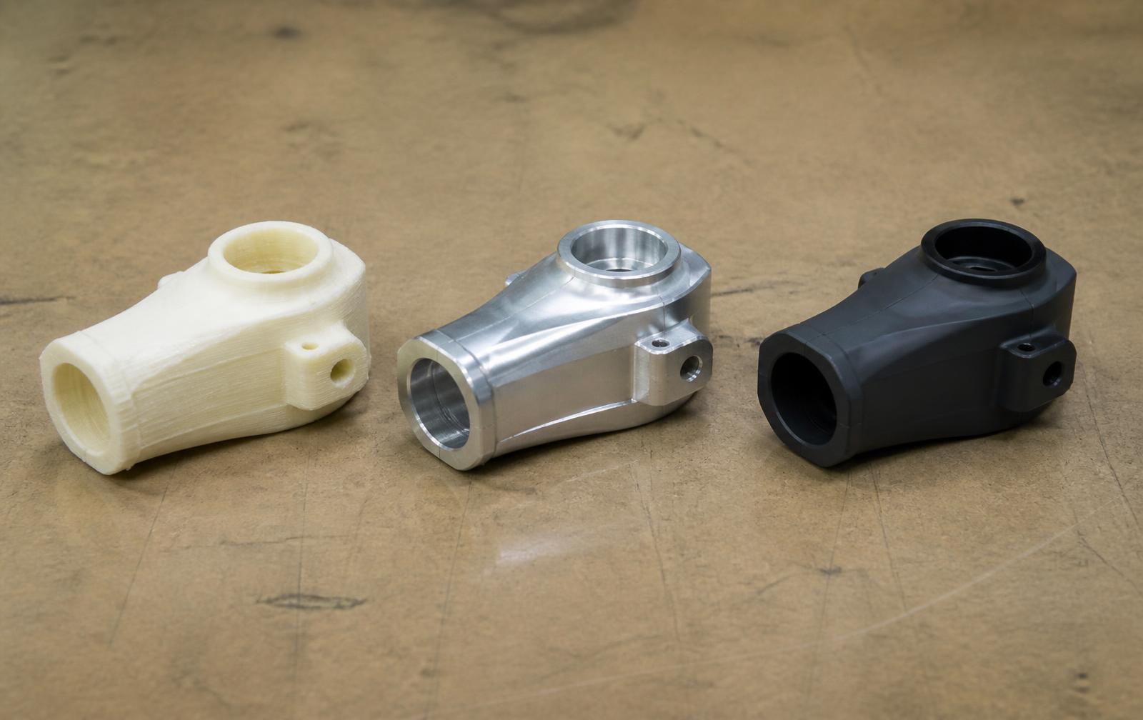 Three versions of the same part: 3D printed white prototype, machined aluminum version, and finished molded black production part