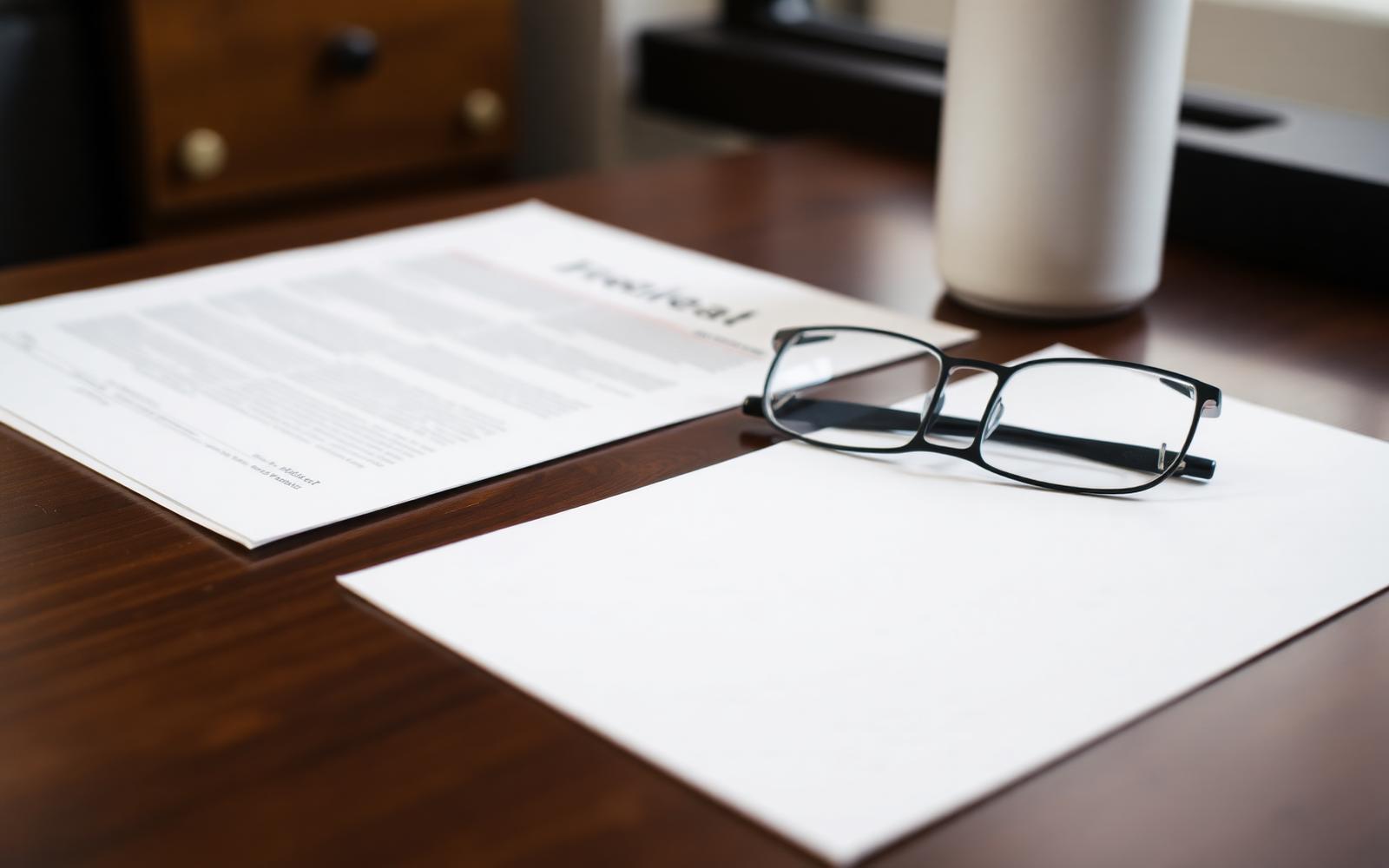 Legal filing paperwork, notepad and reading glasses on a wooden desk during a trademark application review